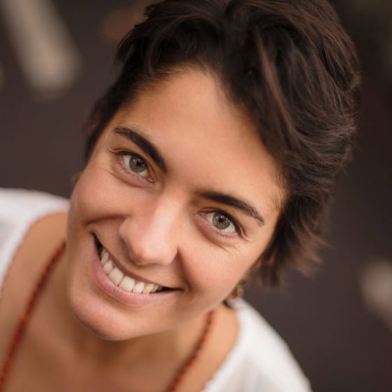 Sorriso feliz de uma mulher com cabelo curto, prestes a fazer uma sessão de yoga ou bem-estar no Lotus Studio, promovendo relaxamento, saúde mental e equilíbrio corporal.